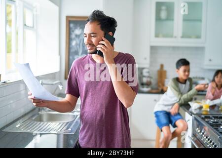 Father talking on smart phone in kitchen with kids Stock Photo