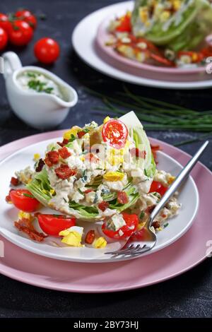 close-up of iceberg wedge salad topped with blue cheese dressing, crispy fried bacon, cherry tomatoes, hard-boiled eggs, chives on plates on a concret Stock Photo