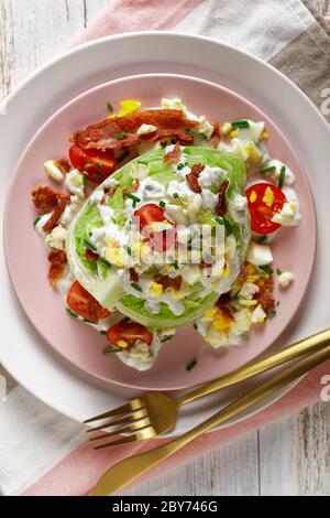 iceberg wedge salad with blue cheese dressing, crispy fried bacon, cherry tomatoes, crumbled hard-boiled eggs, chives on pink plates with golden cutle Stock Photo