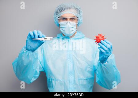 Photo of guy expert doc virologist hold covid bacteria vaccine research show thermometer wear mask hazmat blue uniform surgical cap suit plastic Stock Photo
