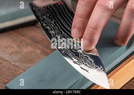 Close-up on a Damascus steel blade being sharpened with a whetstone Stock Photo