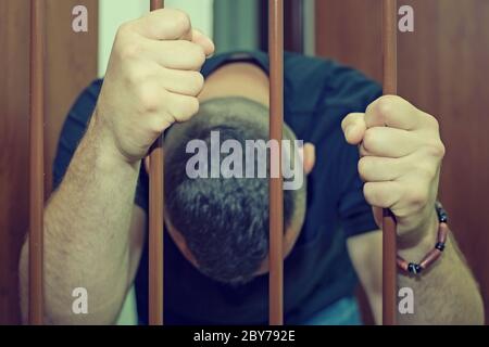 Hands of the prisoner on a steel lattice close up. Prison, man in handcuffs. Assassin, a murderer behind the bars. Abstract. Stock Photo