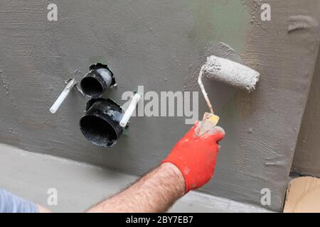 Close-up of an experienced construction worker applying damp insulation with a paint roller on a wall. Stock Photo