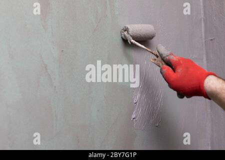 Close-up of an experienced construction worker applying damp insulation with a paint roller on a wall. Stock Photo