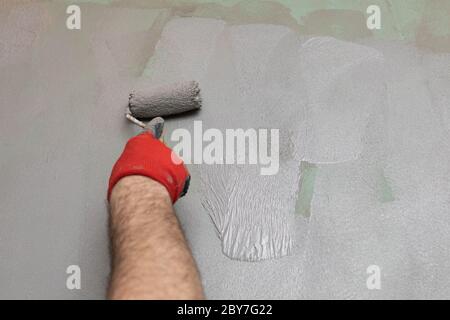 Close-up of an experienced construction worker applying damp insulation with a paint roller on a wall. Stock Photo
