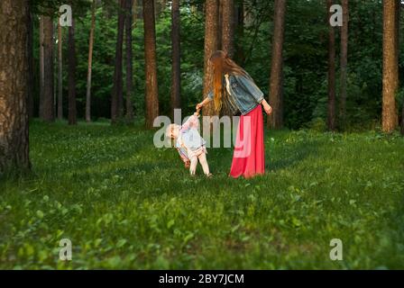 woman with little toddler daughter walk and dance on the lawn in the park Stock Photo