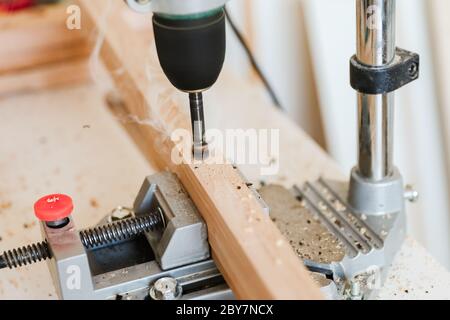 Woodworking with a vertical drill to drill a hole in a wooden block with wood shavings and smoke in a woodworking workshop close-up power tool Stock Photo