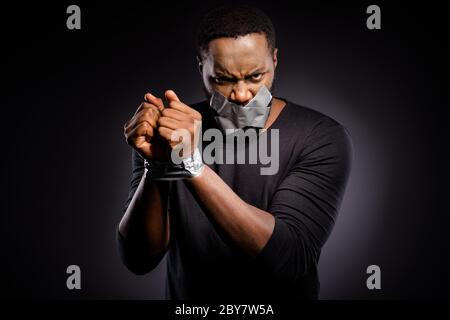 Photo of furious mad afro american guy restrained adhesive tape hand lips close cover suffer no talking speaking injustice isolated over black color Stock Photo