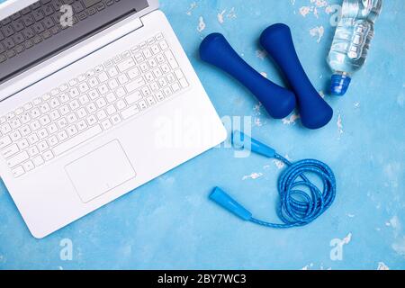 Online fitness workout concept top view. Laptop on the table for stream of sport exercises, dumbbells, jump rope, bottle of water Stock Photo