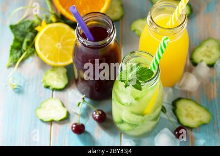 Summer various refreshments drinks. Cherry juice, detox cucumber water and orange juice on blue wooden table. Stock Photo