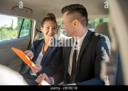 Joyful woman showing tablet to man sitting in car
