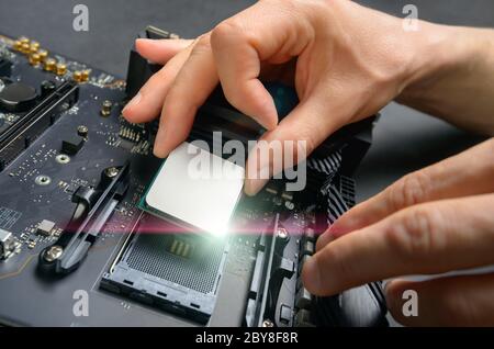 Hands of a technician assembling computer hardware parts, as a new shiny cpu is being mounted unto the motherboard, studio closeup Stock Photo