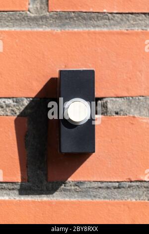 A close up straight portrait of a black and white old plastic doorbell on a red brick wall. The device is ready to be used for someone to announce tha Stock Photo