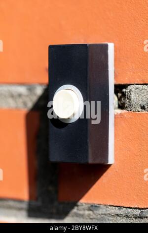 A close up portrait of an old electric doorbell on a red brick wall. The device is black with a white button to ring the bell. Stock Photo