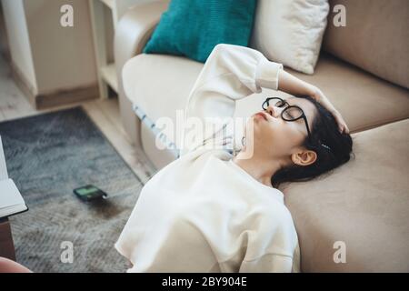 Tired caucasian woman with eyeglasses doing homework on the floor and listen to music from earphones Stock Photo