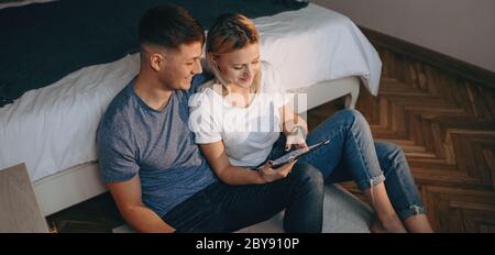 Top view photo of caucasian woman with her lover sitting on the floor and smile while using a tablet Stock Photo