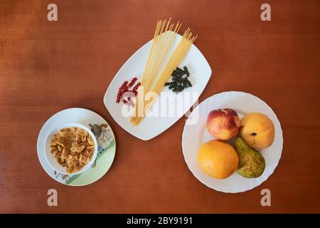 cereals, pasta and fruits on white plates and wooden table Stock Photo