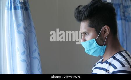 A young asian man mask on his face looking through window  Stock Photo