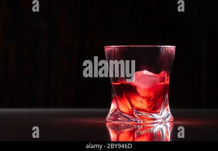 Glass of neat brandy on the rocks with ice cubes on a reflective surface against a dark background in a low angle view with copy space Stock Photo