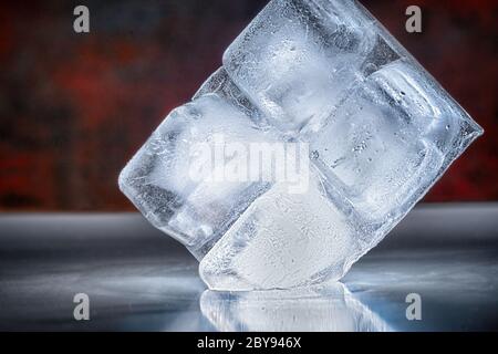 Four ice cubes in a block placed on edge balancing on the corner on a reflective bar counter in a close up low angle view Stock Photo