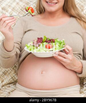 Close up of a future mom eating a salad sitting in the living room Stock Photo