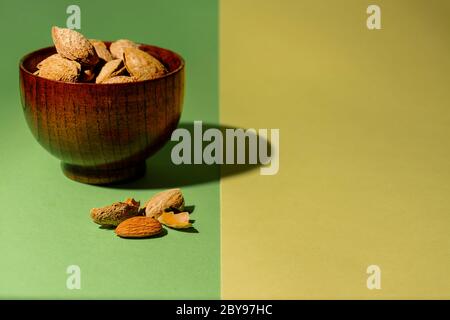 Bowl of raw almonds next to an almond without its shell on a green and yellow background Stock Photo