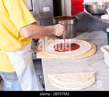 Pizza and pizza making hand putting  spreading sauce on a pizza from a ladle in a circular motion Stock Photo