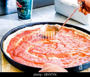 Pizza and pizza making hand putting  spreading sauce on a pizza from a ladle in a circular motion Stock Photo