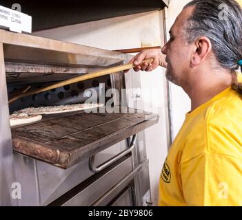 Pizza and pizza making - man placing pizza pie in oven on a wooden  pizza peel Stock Photo
