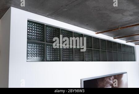A cool-looking low cost glass bricks or glass blocks as a decorative addition in white wall under the ceiling to provide natural daylight, attractive Stock Photo