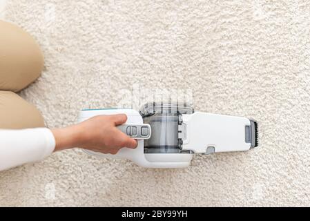 Woman vacuuming furniture in a house with a hand-held portable vacuum cleaner. Stock Photo