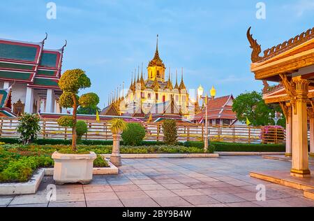 The dimmed lights decorate the scenic building of Loha Prasat temple of Wat Ratchanatdaram complex, seen from topiary Mahajetsadabadin park, Bangkok, Stock Photo