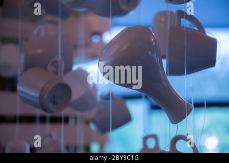 Blue filter photo of kitchen utensil silhouettes. Ceramic vase, coffee cups and tea mugs are hanging on strings in bright sunlight. Morning coffee and Stock Photo