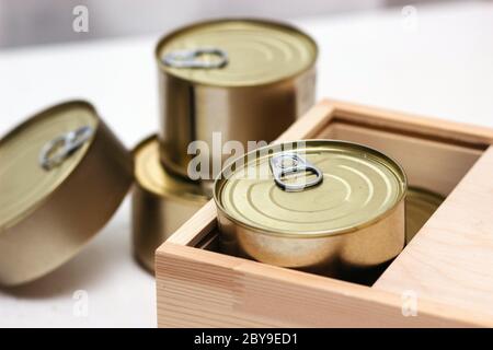 Tin cans in a box. A variety of canned food in full tin cans. Real canned food. View from above. Selective focus Stock Photo