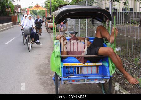 JOGJAKARTA, INDONESIA - JUNE 12, 2013: Rickshaw driver sleeping on the job in the streets of Yogyakarta, Indonesia. Becak taxi with driver person slee Stock Photo