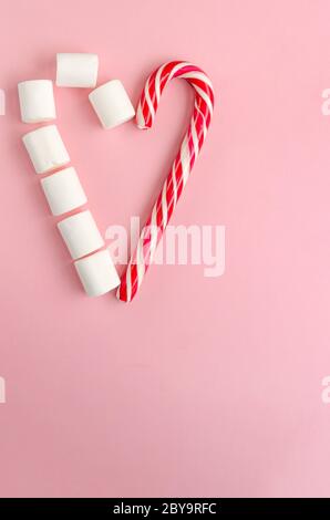 Heart shape made of candy cane and white marshmallows on pink background. Christmas, Valentines day concept. Festive background Stock Photo