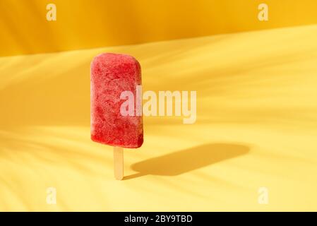 Homemade fruit ice cream popsicle on a yellow background in sunlight. Strawberry sorbet on a stick. Tropical summer context.  Refreshing dessert. Stock Photo