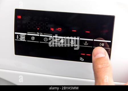 Close Up Of Man Choosing Cycle Program On Washing Machine. Adjusting wash settings on the control panel of washing machine. Smart home concept. Stock Photo