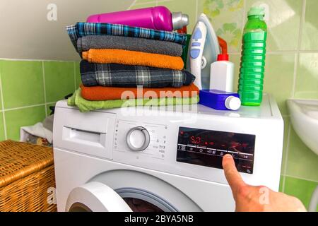 Close Up Of Man Choosing Cycle Program On Washing Machine. Adjusting wash settings on the control panel of washing machine. Smart home concept. Stock Photo