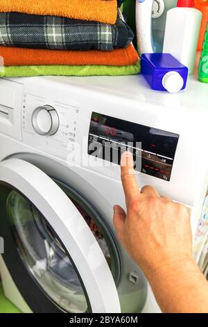 Close Up Of Man Choosing Cycle Program On Washing Machine. Adjusting wash settings on the control panel of washing machine. Smart home concept. Stock Photo