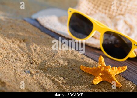 A summer hat and sunglasses lie on the sandy coast of the sea beach. Stock Photo