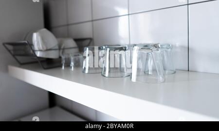 Wide kitchen shelves and wall shelving for storage and display. White wooden shelf and budget lightweight dish rack with dishes, cups and glasses Stock Photo
