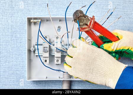 Installation of switchboard with automatic fuses in household wiring network. The installer cuts the ends of the copper wires with the help of end cut Stock Photo