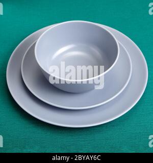 A set of kitchen utensils, two plates of different sizes and a bowl. Ceramic dishes with gray glaze. Dinnerware on a green background. Stock Photo