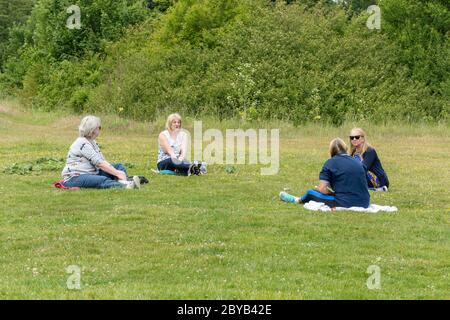 A group of four women sitting in a park with social distancing, 2 metres apart, after the coronavirus covid-19 lockdown has been eased, UK, June 2020 Stock Photo