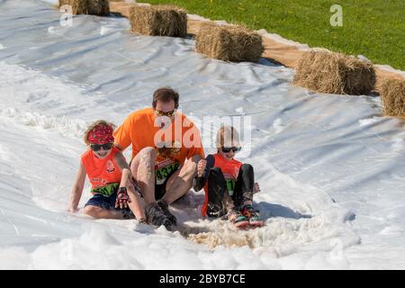 Poley Mountain, New Brunswick, Canada - June 10, 2017: Participating in the annual fundraiser 'Mud Run For Heart'. A man and two children slide down a Stock Photo