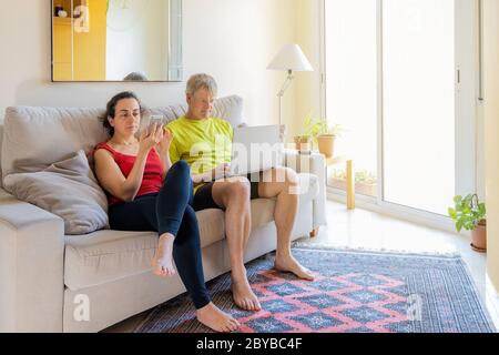 Middle-aged couple sitting on the sofa and communicating with cell phone Stock Photo