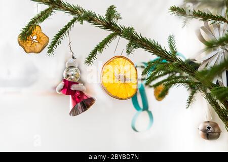 Closeup of decorated retro Christmas tree with hanging decorations as orange or apple slice, red figurine, metal jingle bell and paper chain or flower. Stock Photo