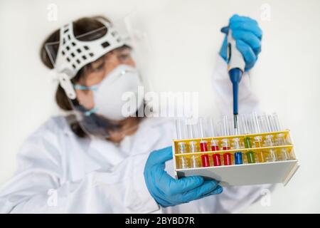 Female laboratory technician holding pipette and glass test tubes in rack. Scientist in protective wear and gloves. Colored liquids in lab equipment. Stock Photo