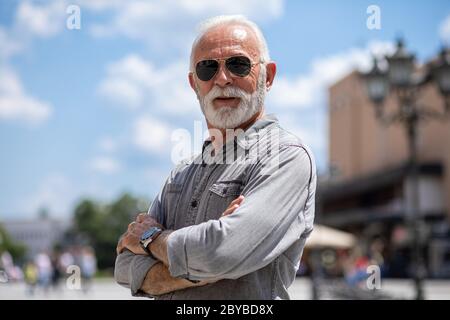 Experienced senior old man with beard and sunglass on street posing and smiling, portrait Stock Photo